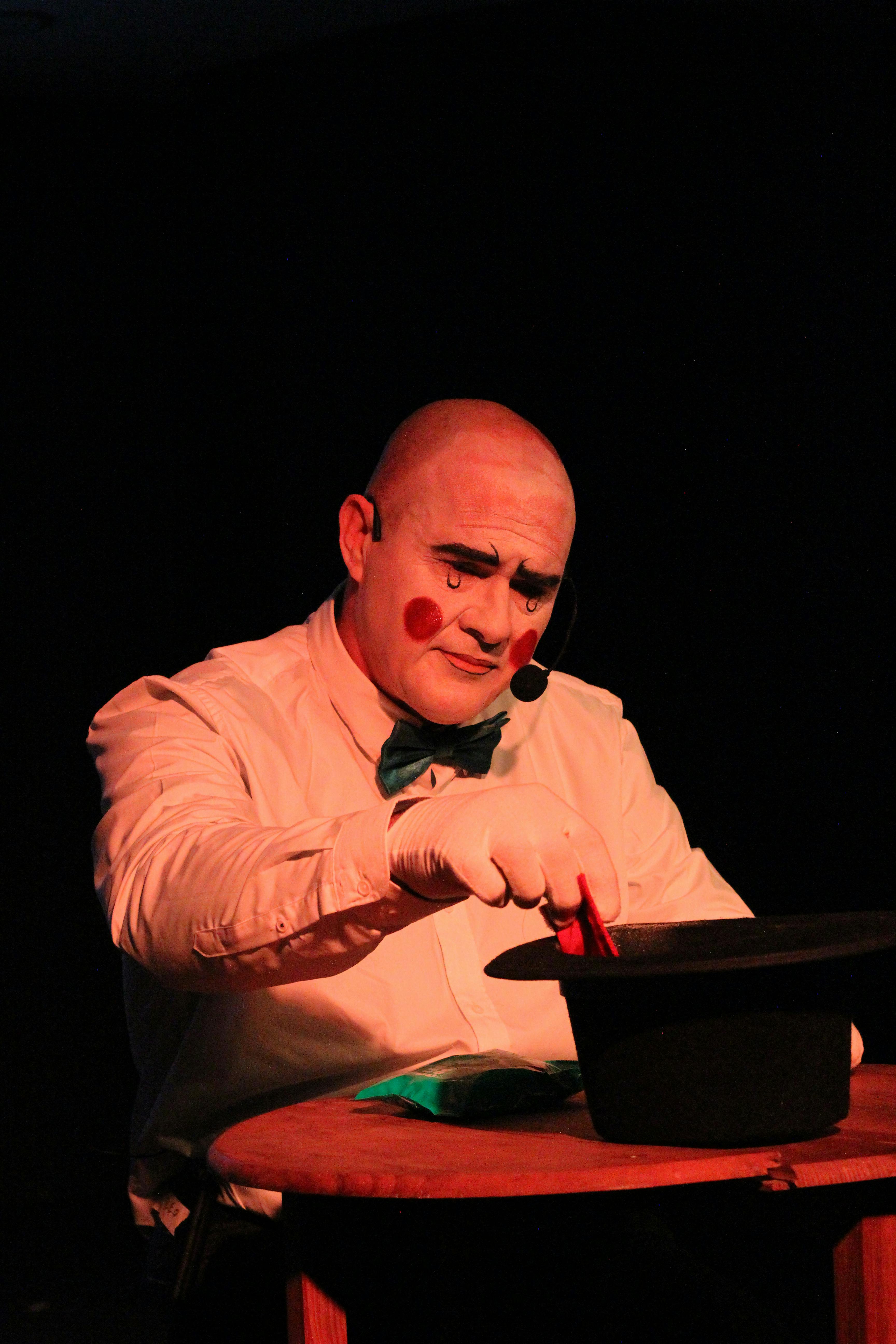 Gratis Un mago con cara de payaso realizando un truco de magia con un sombrero en el escenario. Foto de stock