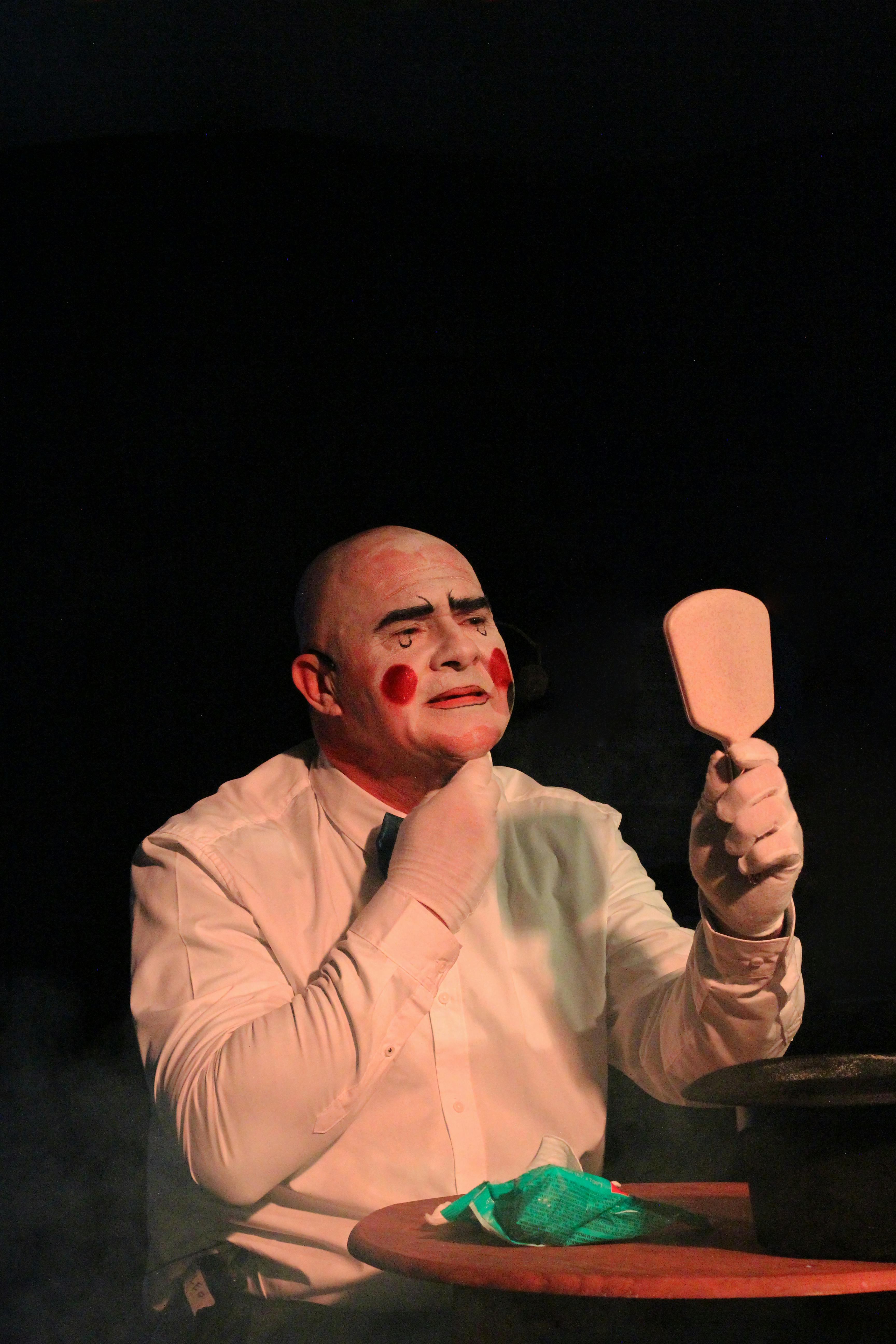 Gratuit Un clown se maquille, se reflétant dans un miroir sous un éclairage théâtral. Photos