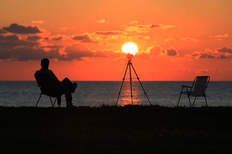 Silhouette Of Man Sitting On Chair Near Sea During Sunset