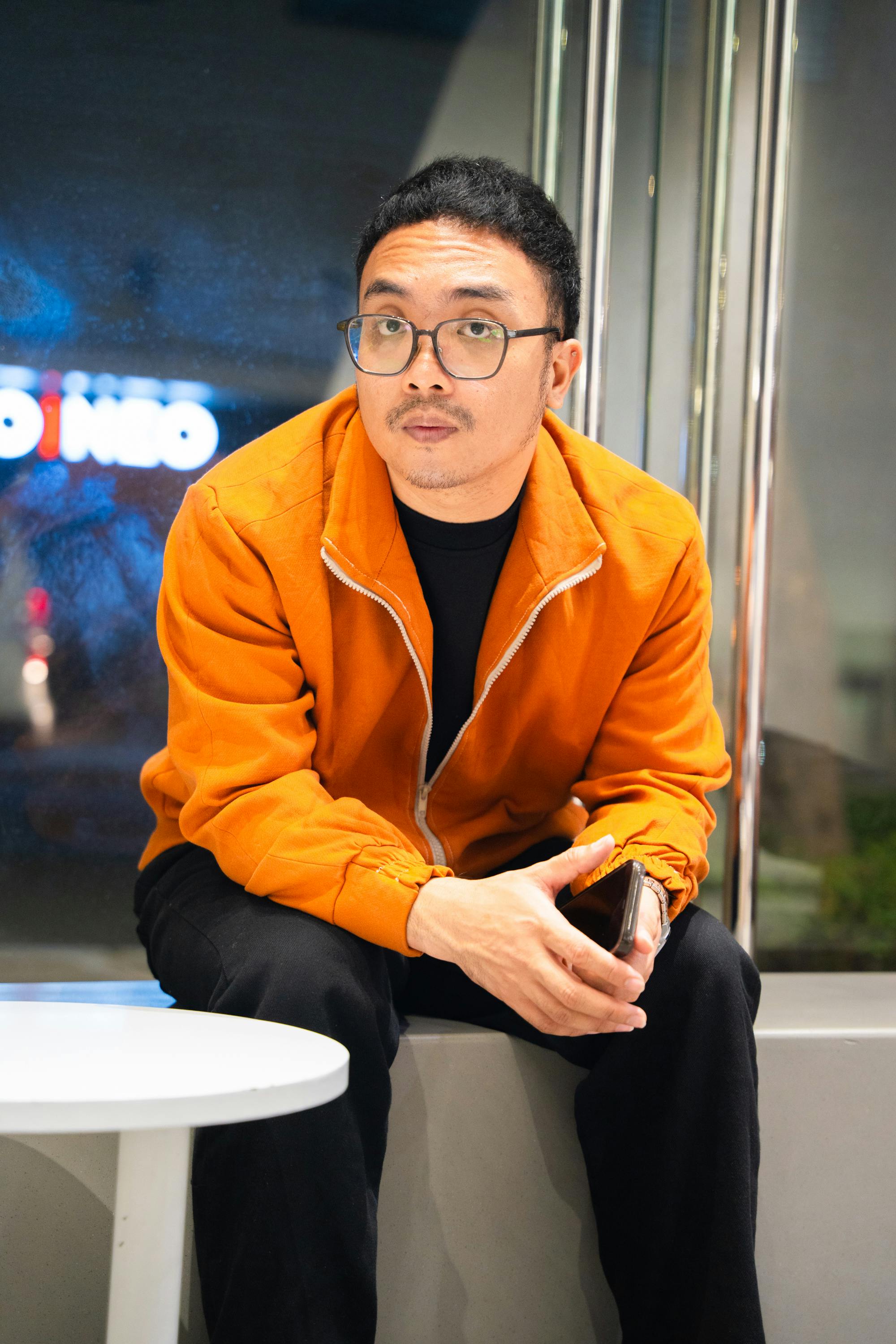 Casual portrait of a man sitting indoors wearing an orange jacket.