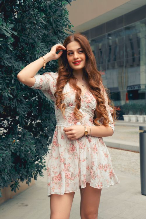 Free Young woman with flowing hair in a floral dress stands gracefully in an outdoor setting. Stock Photo