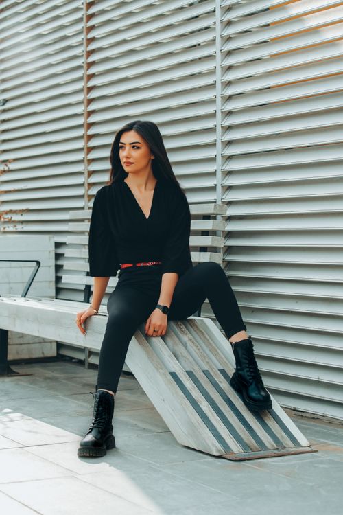 Free Stylishly dressed woman sitting outdoors in urban setting, conveying modern fashion. Stock Photo