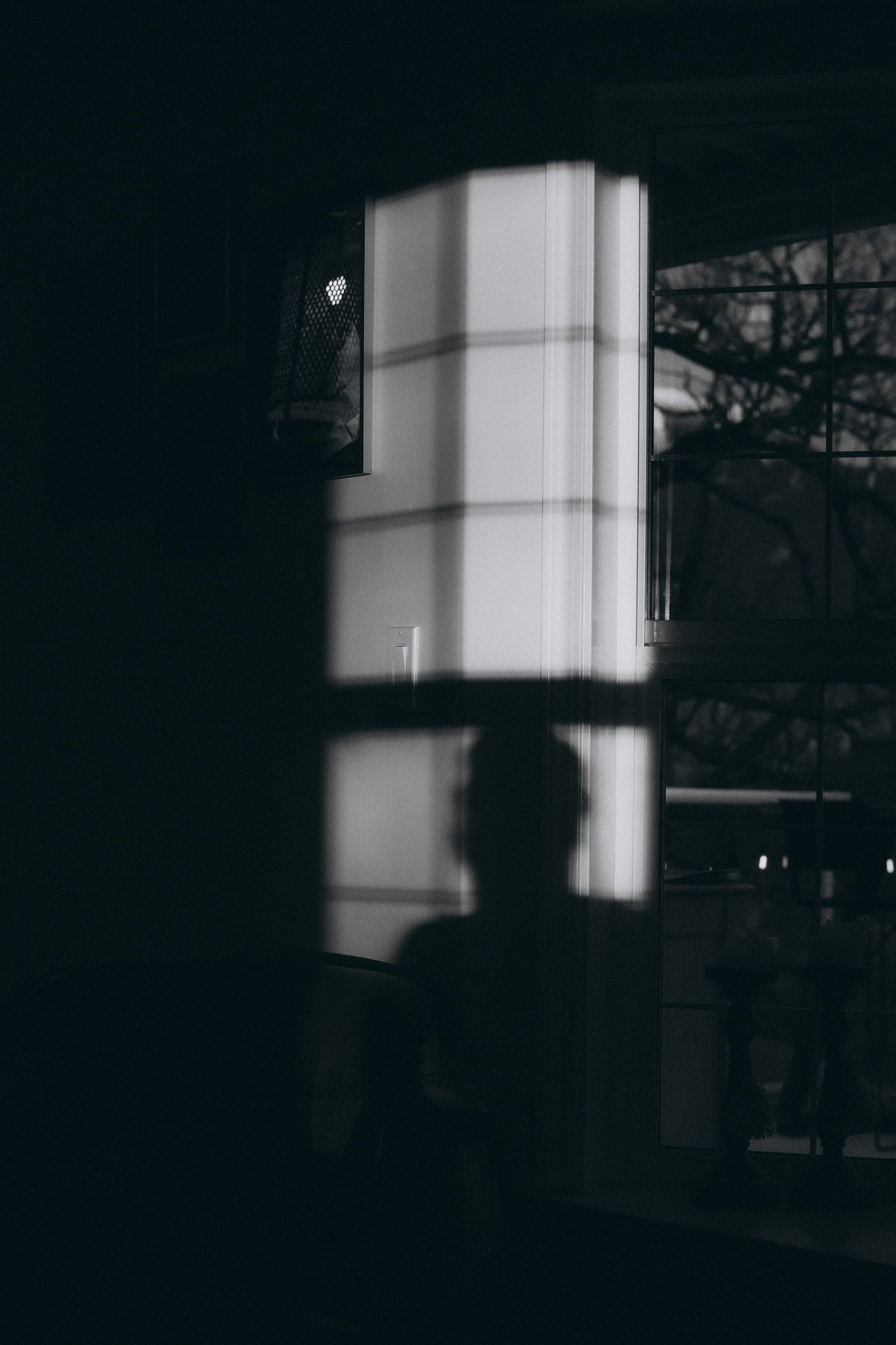 Kostnadsfria En dramatisk siluett gjuten av fönsterljus på en svagt upplyst vägg som framkallar mystik. Stock foto