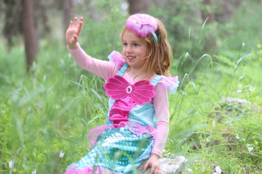 Cute child in mermaid costume waving in a lively outdoor park setting.