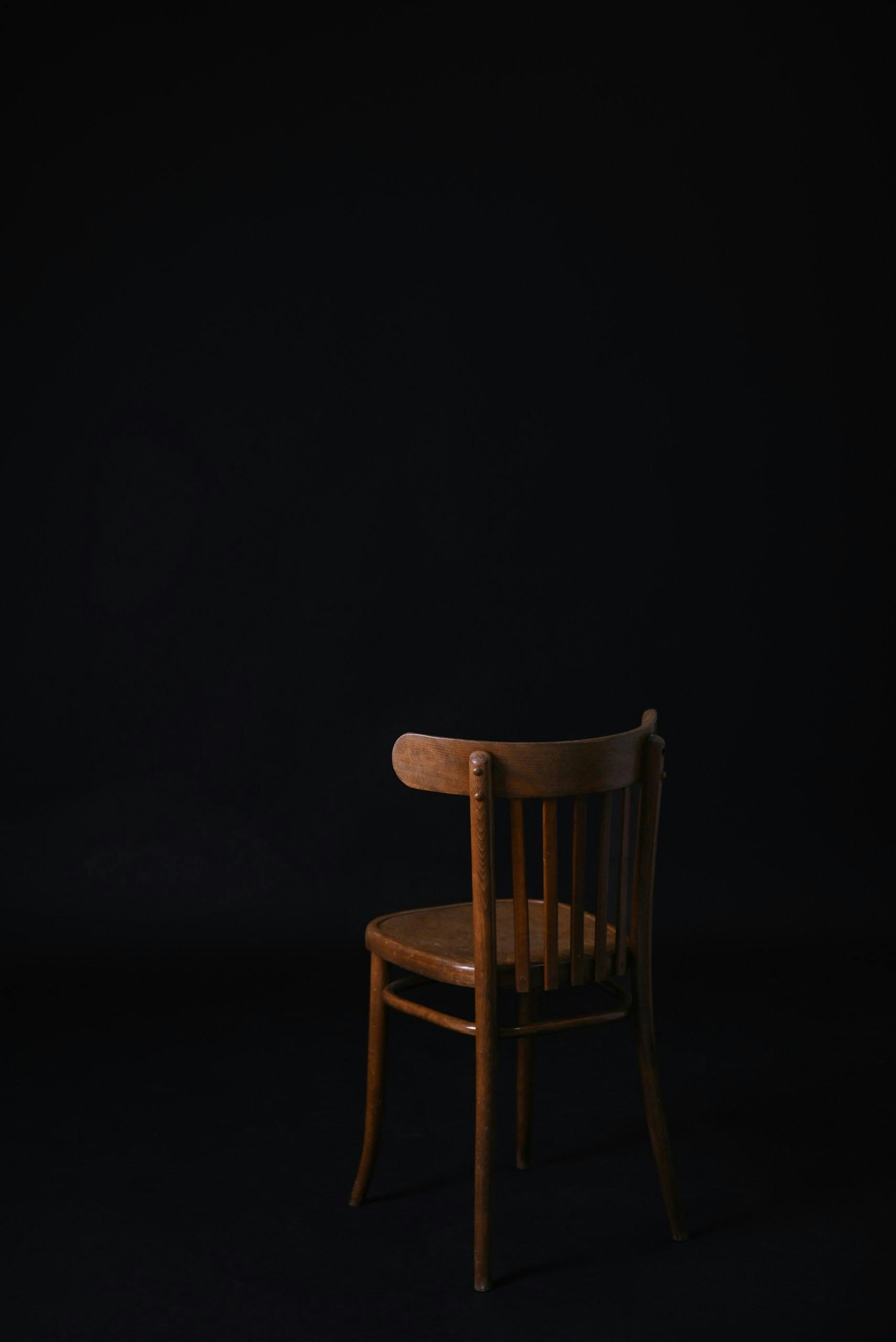 ingyenes Egy magányos fából készült szék sötét háttér előtt, amely az egyszerűséget és az eleganciát hangsúlyozza. Stockfotó