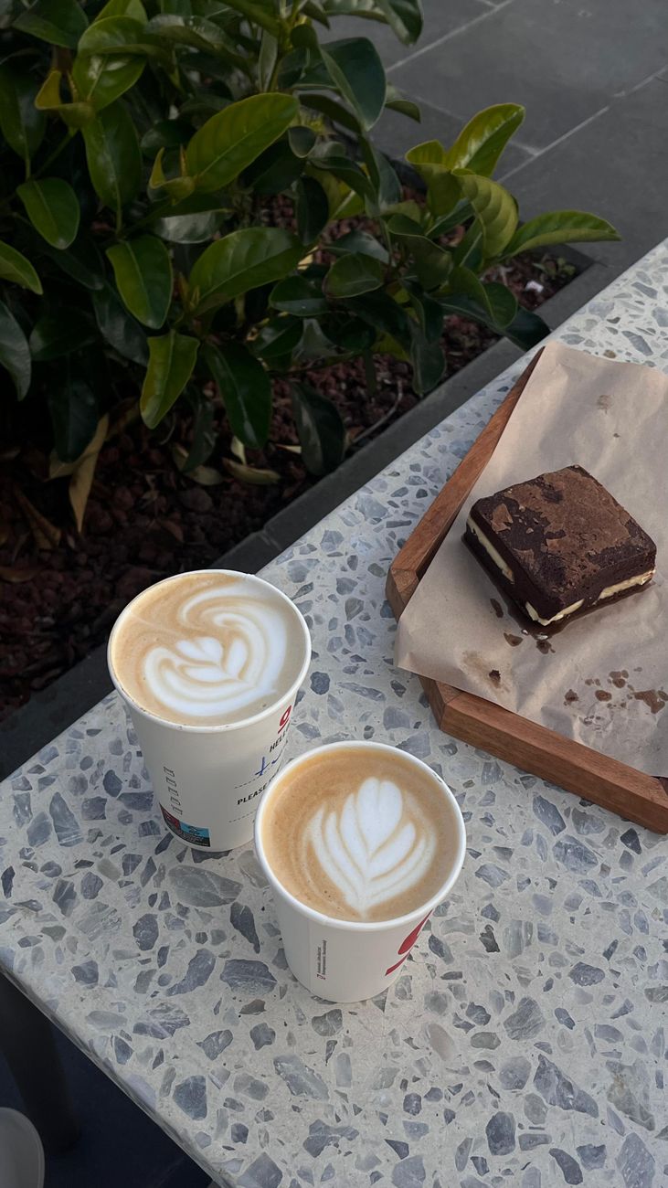 Two lattes with latte art and a chocolate dessert on an outdoor cafe table.