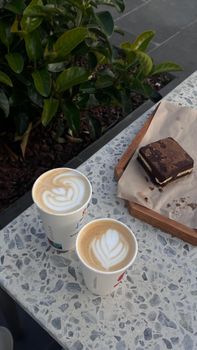 Two lattes with latte art and a chocolate dessert on an outdoor cafe table.