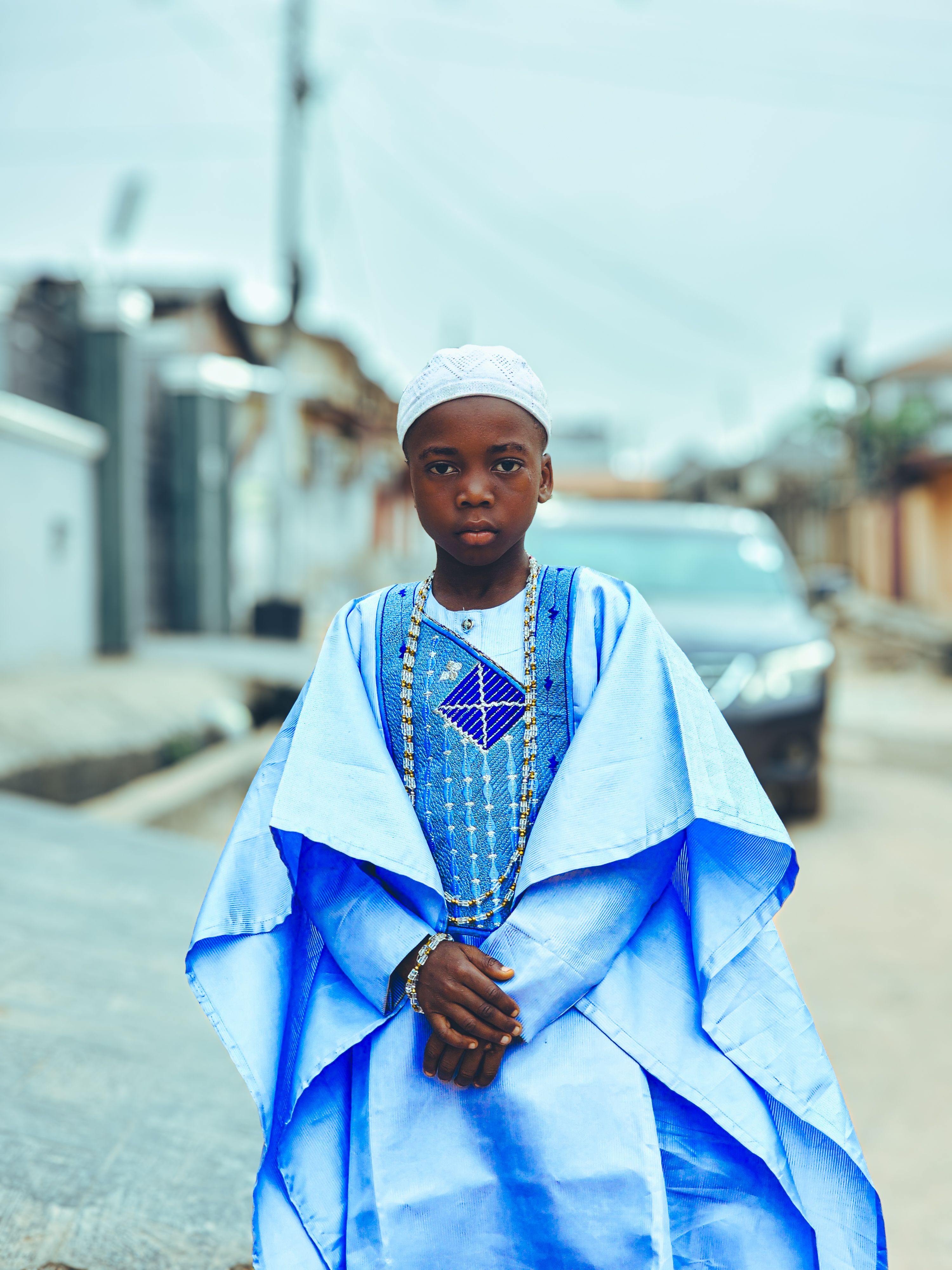 A young boy stands confidently in traditional blue attire on an outdoor street scene.