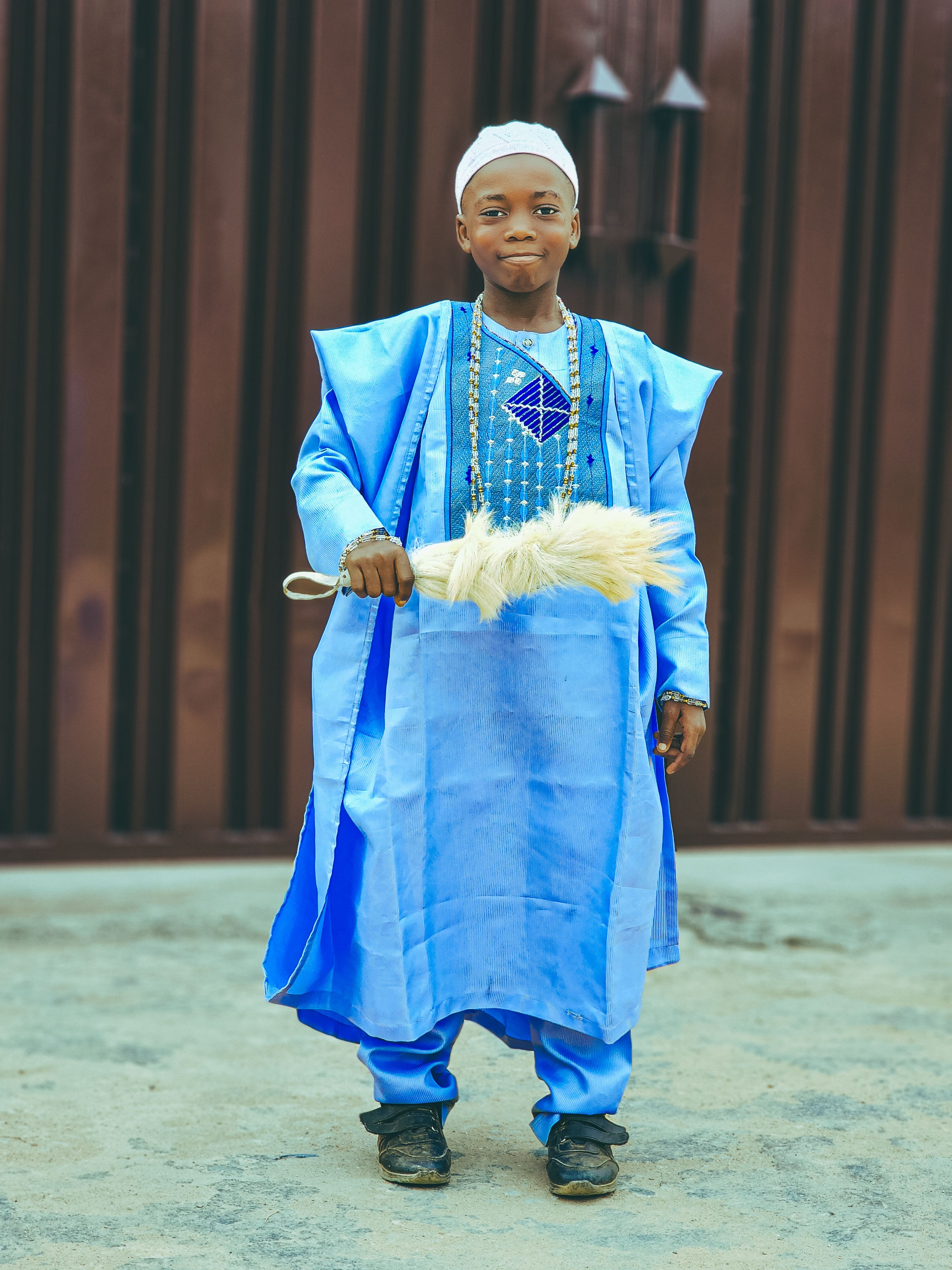 A young boy dressed in vibrant traditional African clothing, standing outdoors.