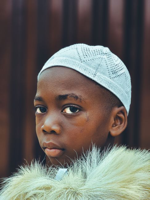 Close-up portrait of a young boy wearing a white cap and fur coat.