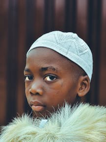 Close-up portrait of a young boy wearing a white cap and fur coat.