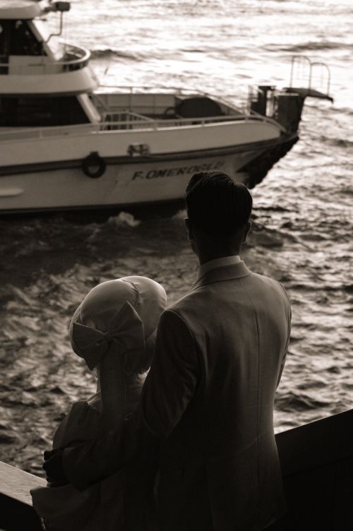 Free Bride and groom in vintage attire watching a boat on a river, in sepia tone. Stock Photo