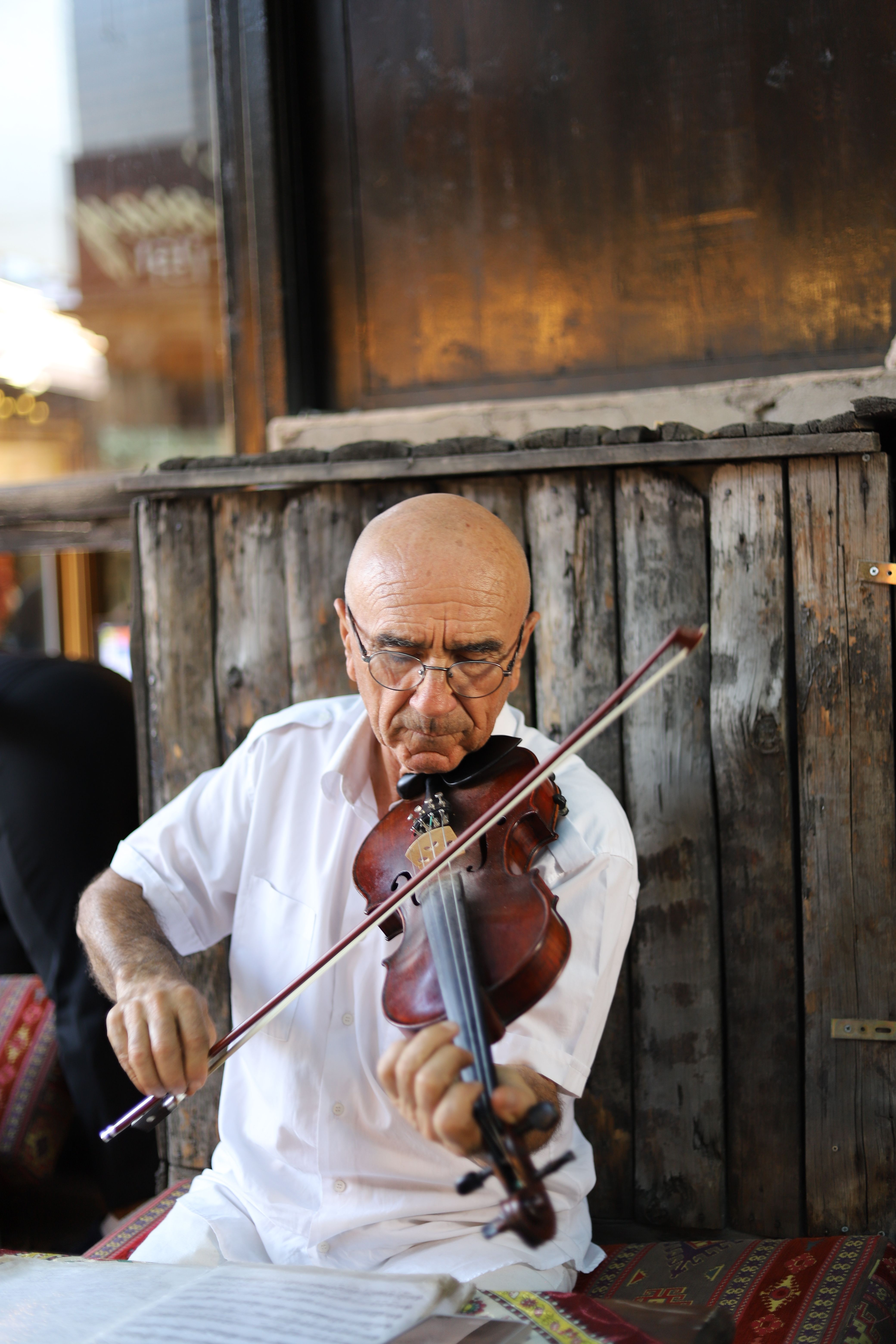 Elderly man in white shirt passionately playing violin outside.