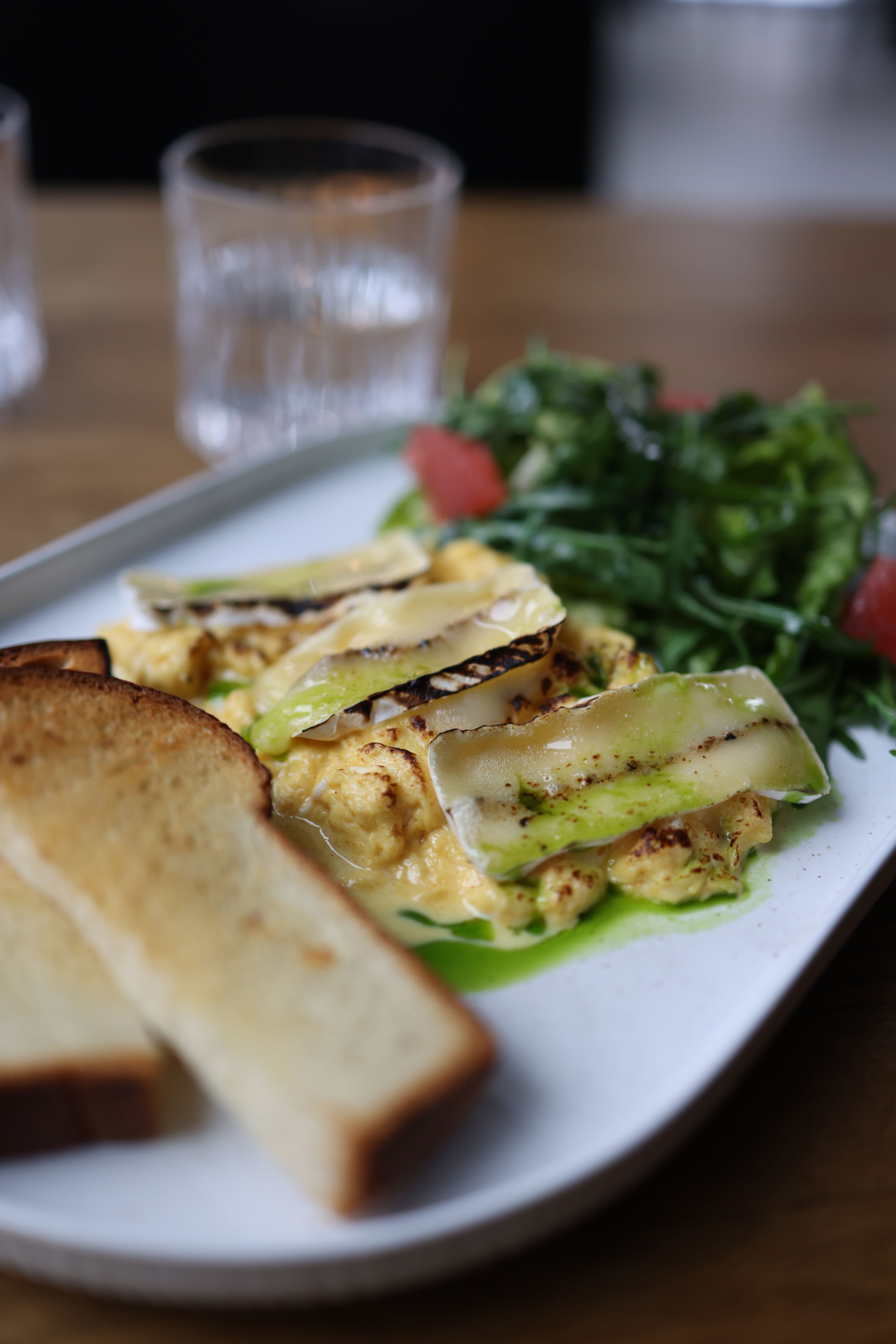 Delicious scrambled eggs with grilled veggies, toast, and salad on a plate.