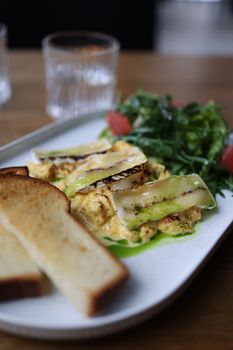 Delicious scrambled eggs with grilled veggies, toast, and salad on a plate.
