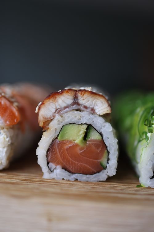 Free Close-up of a sushi roll with salmon, eel, avocado, and rice on a wooden board. Stock Photo