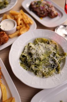 Close-up of green pasta with parmesan cheese on a table with fries and sauce.