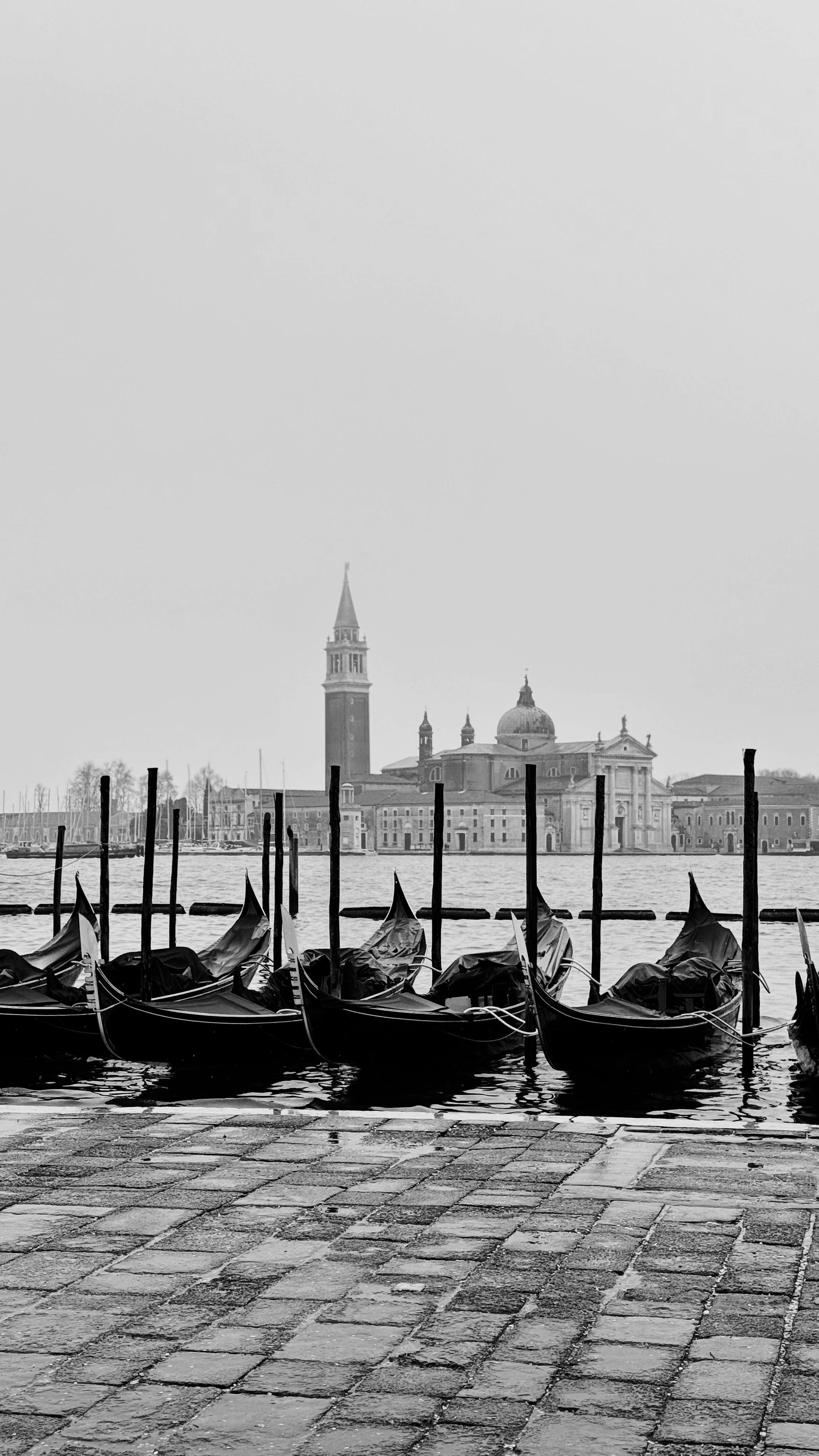Black and white photo of gondolas with Venetian skyline, capturing timeless elegance.