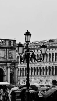 Black and white photo of a street lamp and crowd with umbrellas in Venice, Italy.