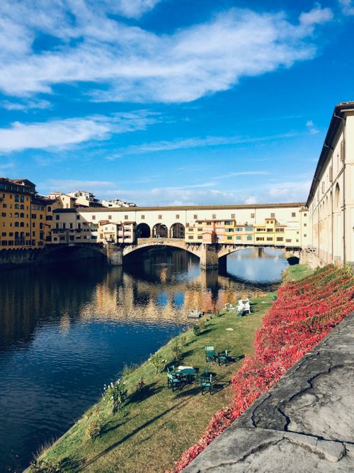 Free Scenic view of Ponte Vecchio over Arno River in Florence, Italy, showcasing vibrant autumn foliage. Stock Photo