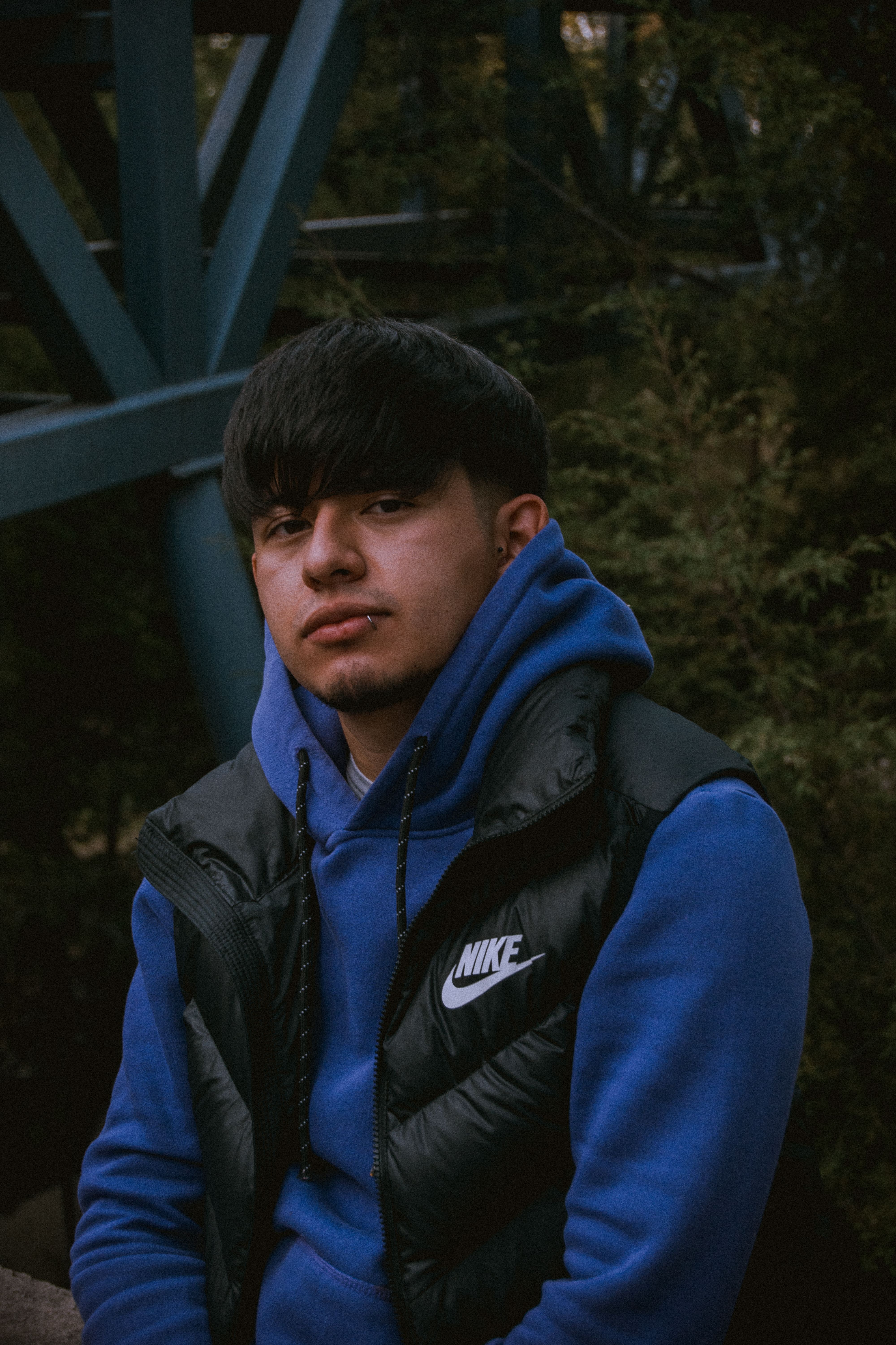 Portrait of a young man wearing a blue hoodie, outdoors with a dark, moody background.