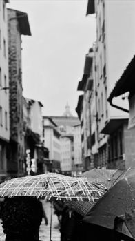 Monochrome shot of umbrellas in a narrow European street on a rainy day.