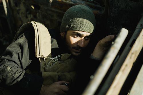 Free A man in a beanie and military vest sits in a low-light, shadow-filled environment. Stock Photo