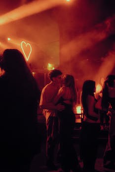 A couple embracing in a lively club illuminated by heart-shaped neon lights, capturing a romantic moment.