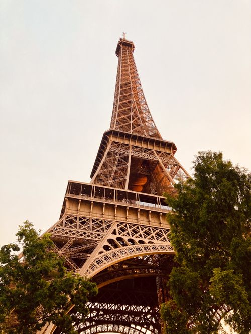Free Low-angle view of the Eiffel Tower against a warm sunset sky in Paris, France. Stock Photo