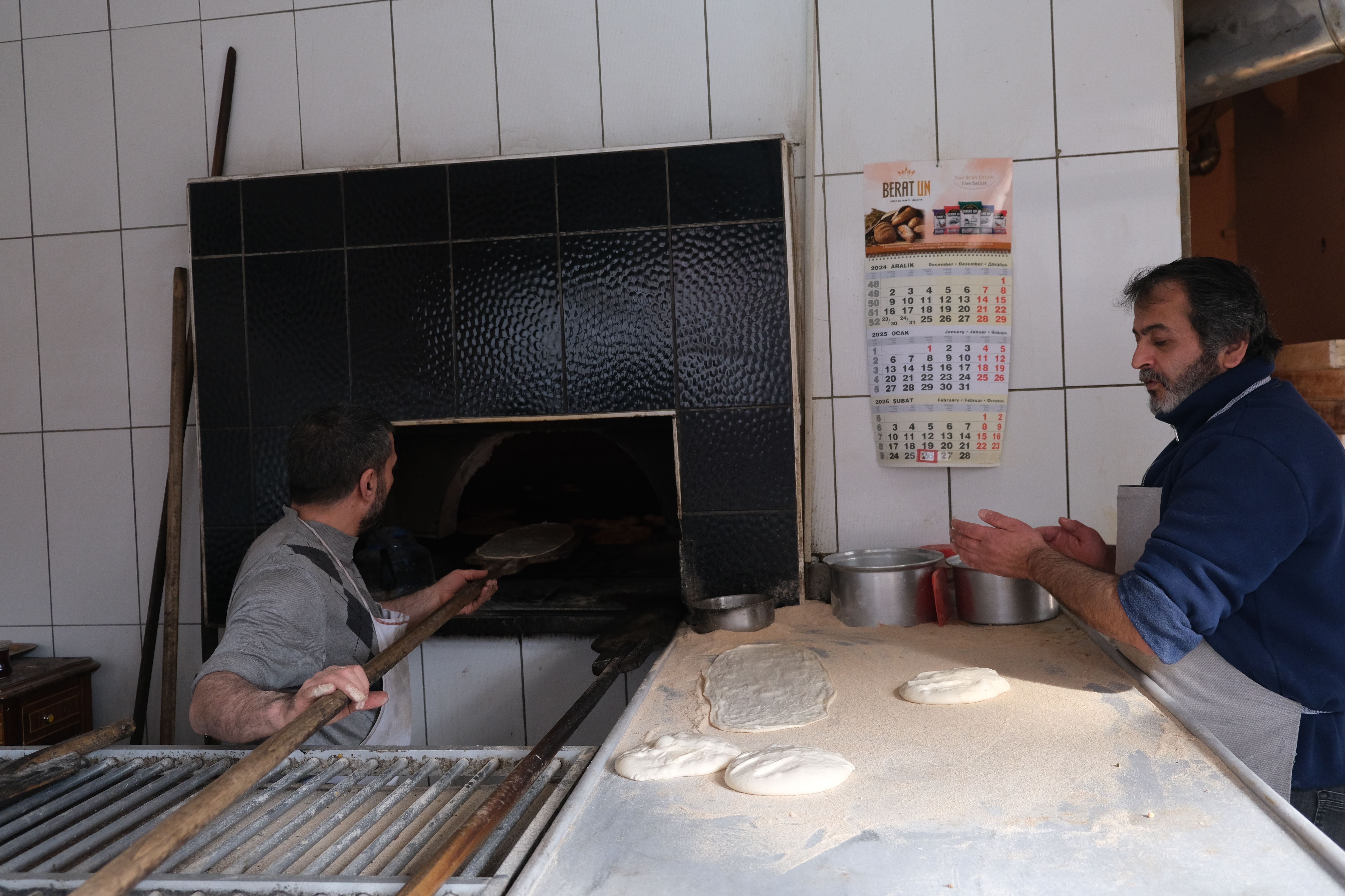 Bakers working with dough in a traditional bakery with a wood-fired oven.