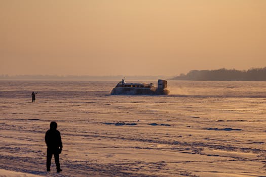 Hovercraft traversing frozen landscape during sunset, creating a serene winter scene.