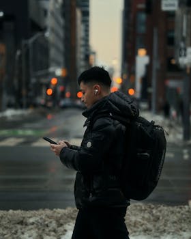 Man in winter coat walking with phone in Toronto street, bokeh lights.