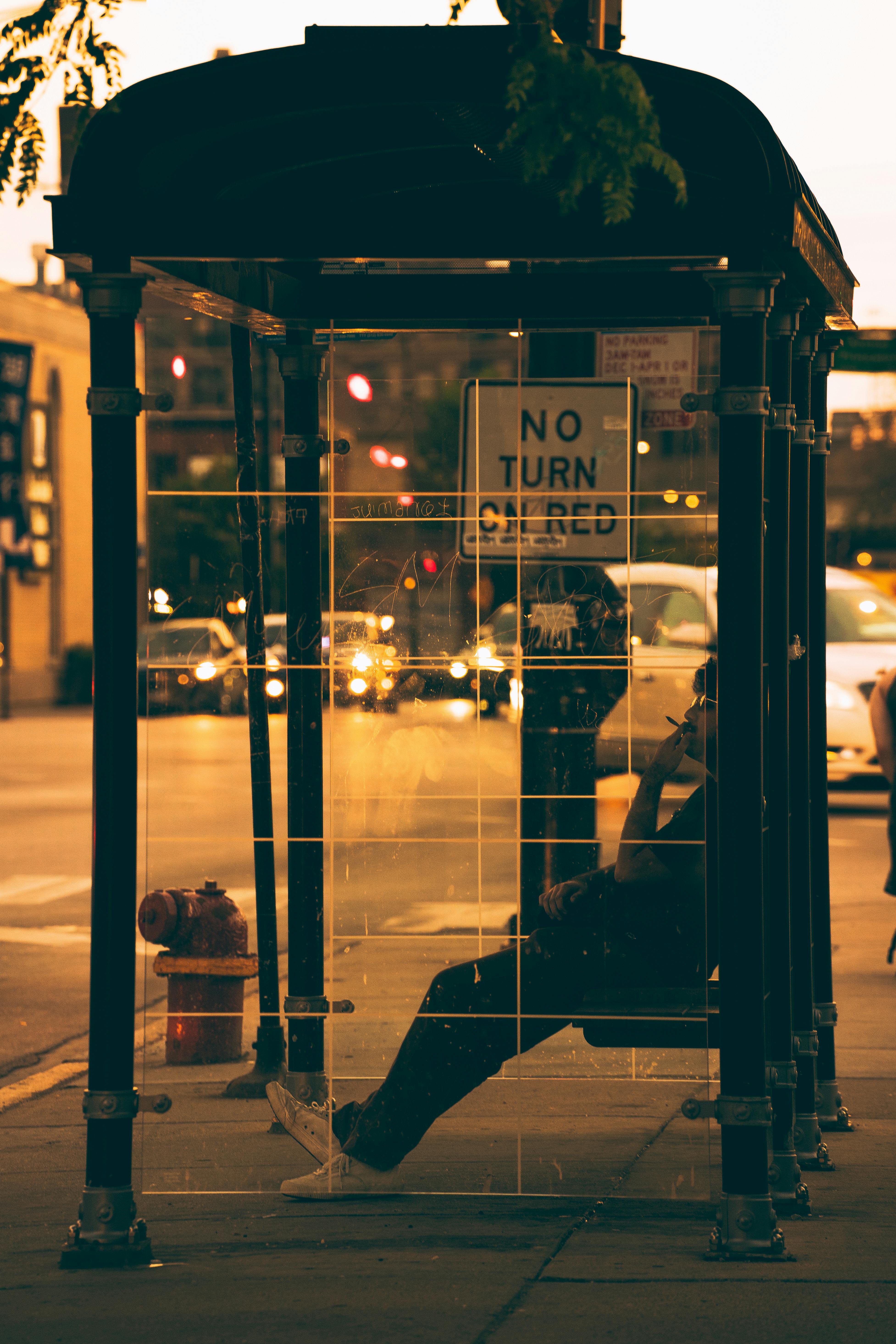 gratis Een persoon zit 's nachts op een bushalte op straat in de stad, terwijl er veel verkeer en lichten voorbijrijden. Stockfoto