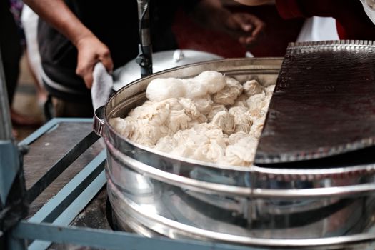 A close-up of steaming dumplings being prepared by vendors at an outdoor street market.