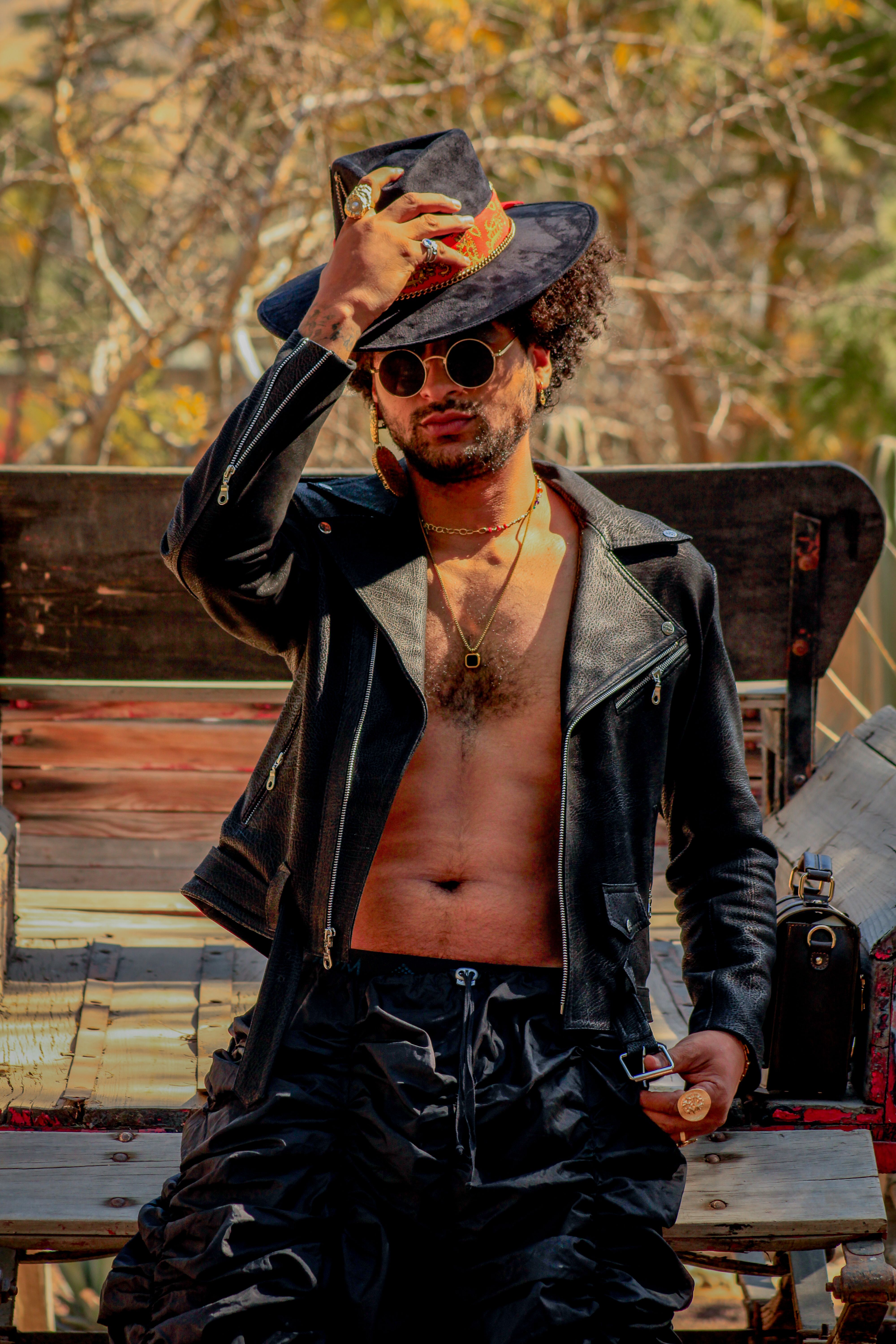 Fashionable man in sunglasses and leather jacket poses with confidence outdoors.