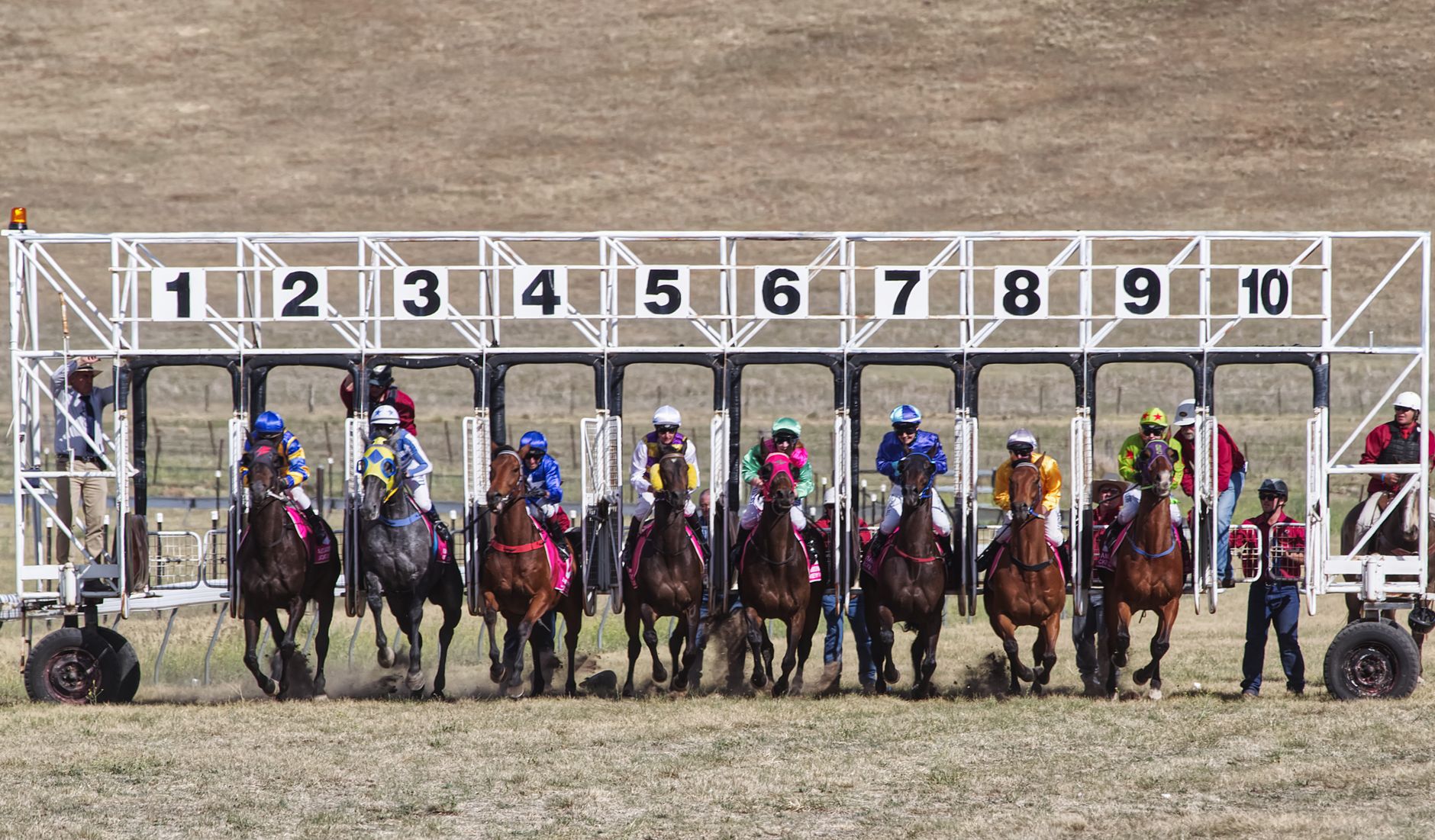 Horses and jockeys burst from the starting gate at a thrilling horse race in Alpine Village, Australia.