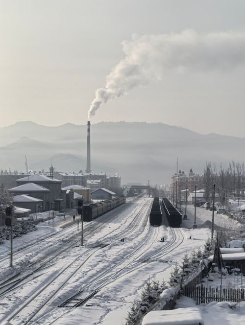 Free A snow-covered railway leads to an industrial smokestack, emitting smoke against a mountainous backdrop. Stock Photo