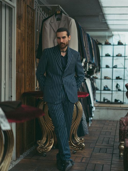 Free Man in a sleek pinstripe suit poses stylishly in a fashion boutique. Stock Photo