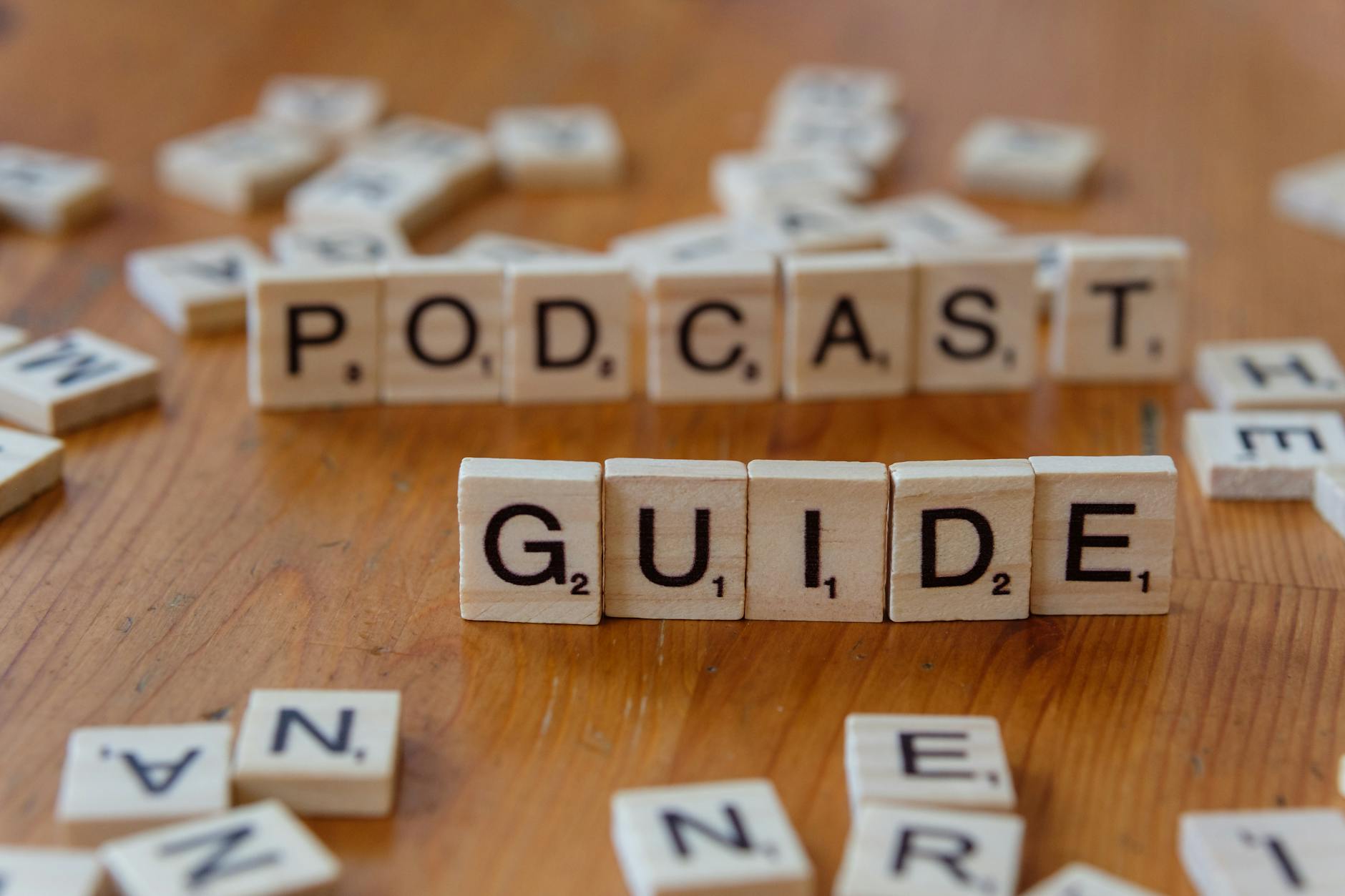 Scrabble tiles forming the words 'Podcast Guide' on a wooden surface.