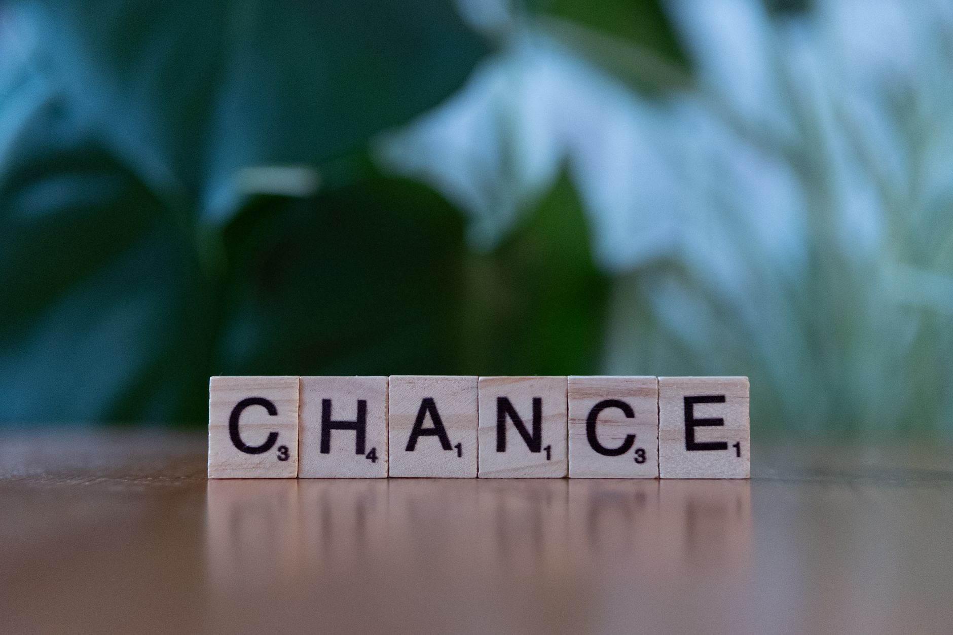 Scrabble tiles spelling 'chance' on a wooden surface with a blurred green background.