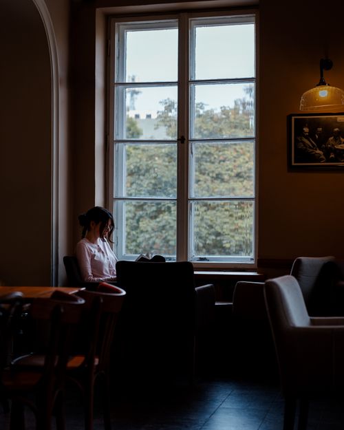 Free A serene scene of a woman reading by the window in a cozy Warsaw cafe, surrounded by a warm atmosphere. Stock Photo