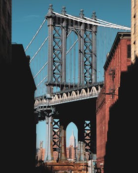 Empire State Building framed by Manhattan Bridge in NYC during daytime.