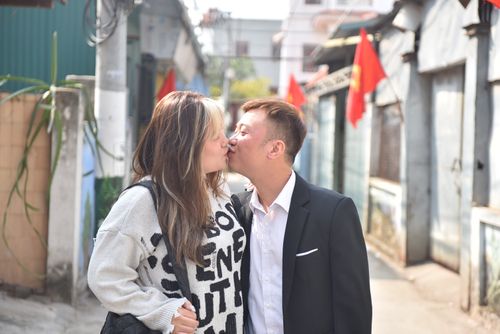 Free A couple shares a tender kiss on a sunny urban street lined with red flags. Stock Photo