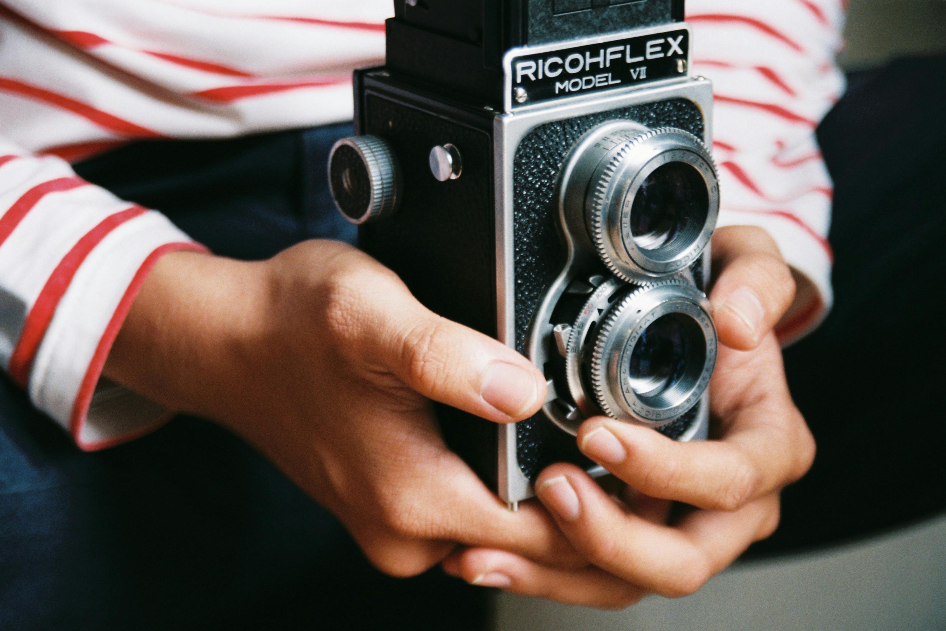 Close-up of hands holding a vintage Ricohflex camera, capturing classic photography charm.