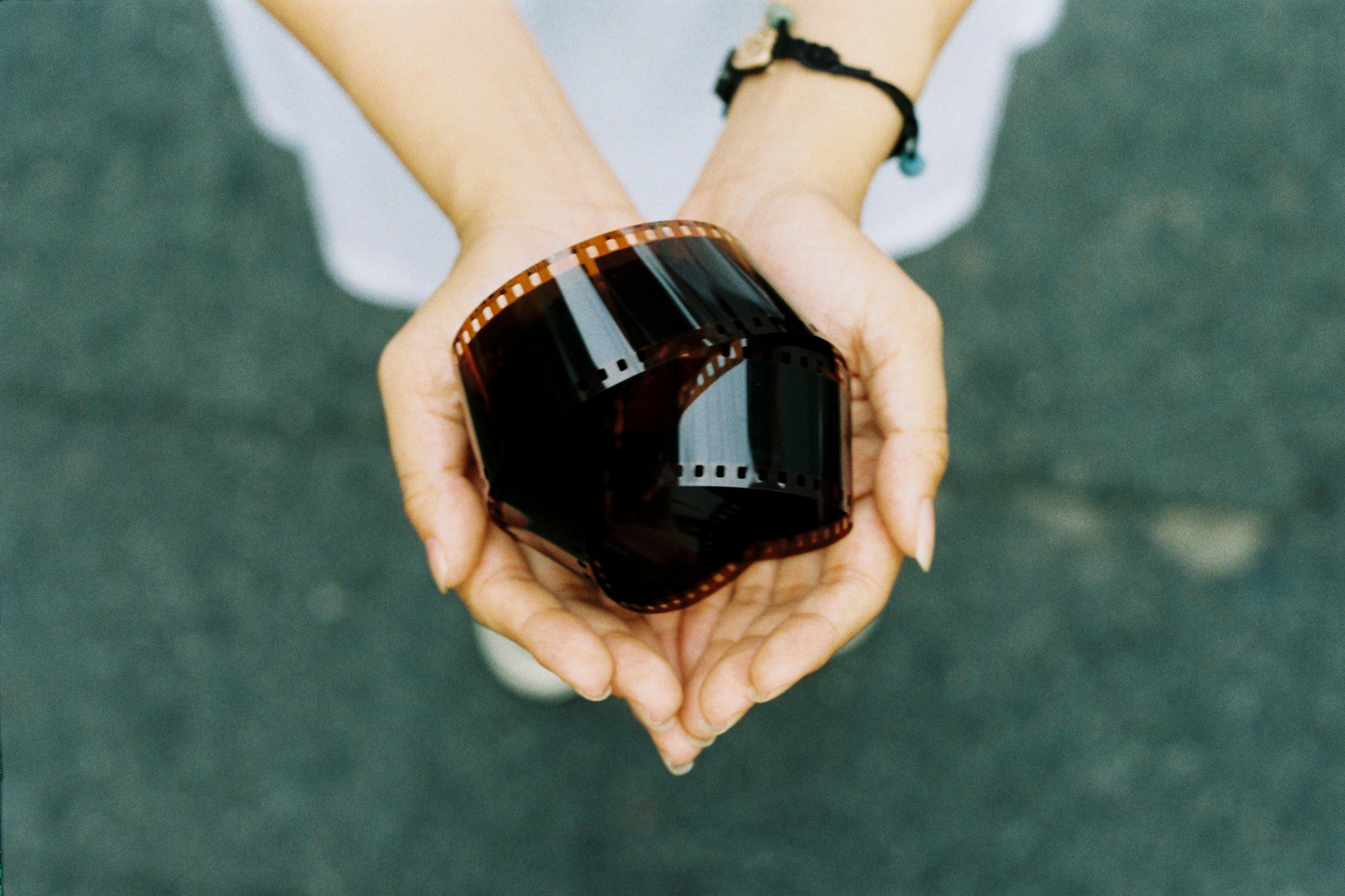 A pair of hands gently holding a curled film roll, captured outdoors in Ho Chi Minh City, Vietnam.