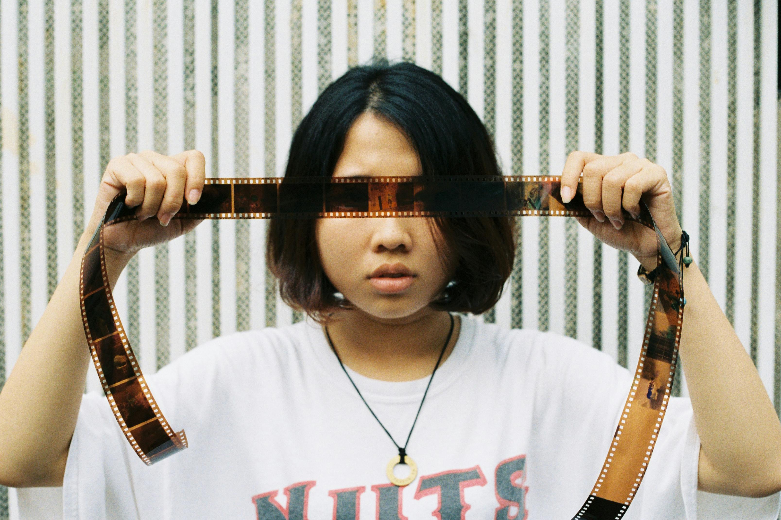 A young woman holding film negatives in front of her face outdoors.
