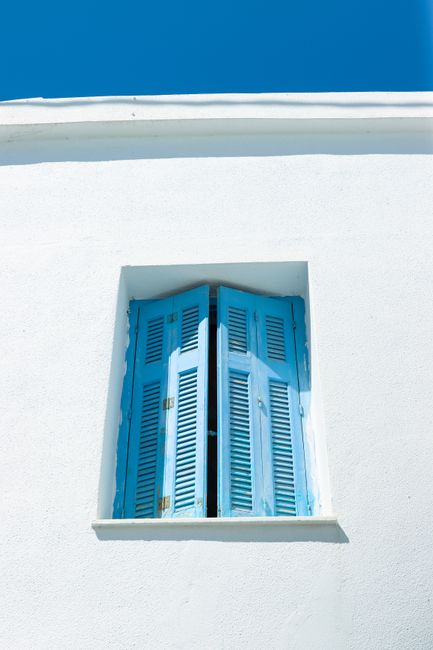 Bright blue shutters on a white wall in Naxos, Greece, under a clear sky.