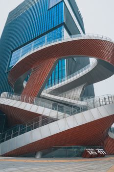 Dynamic spiral staircase outside a modern glass skyscraper in an urban environment.