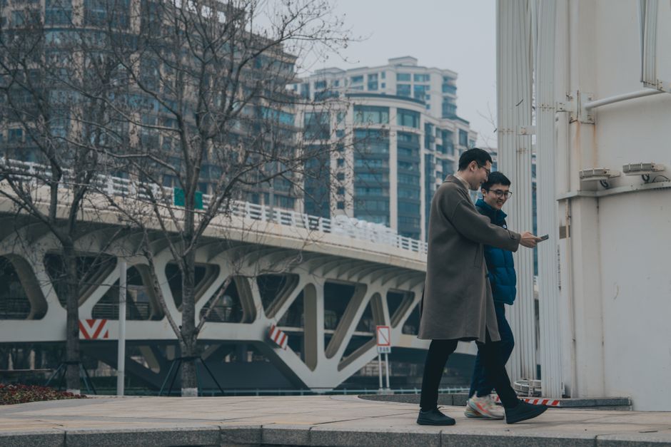 Photo by Neil Ni on Pexels Two men walking near a modern bridge in a cityscape, enjoying a leisurely day outdoors.