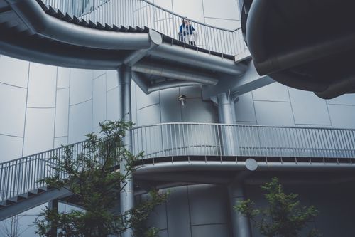 Free A person stands on a futuristic, industrial staircase in a modern urban setting. Stock Photo